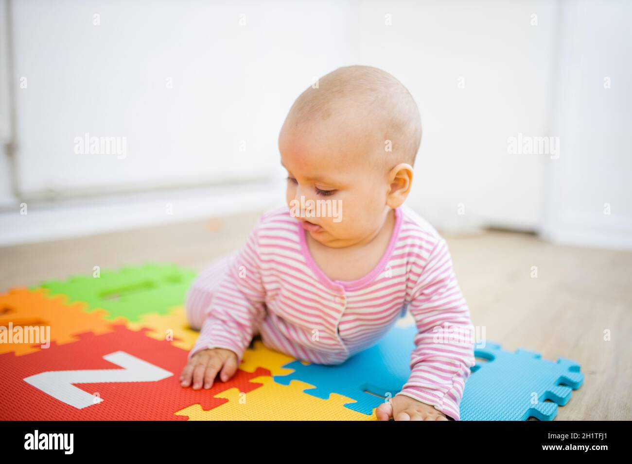 Liebenswert Baby liegt mit dem Gesicht nach unten auf bunten Kinder Matte mit Buchstaben. Porträt von abgelenkt aussehenden Baby auf dem Boden spielen. Glückliche Babys, die Spaß haben Stockfoto