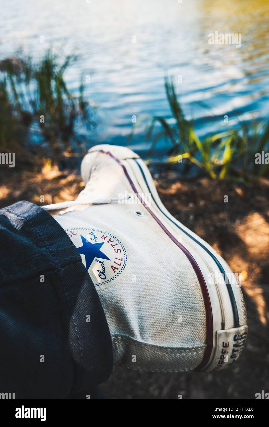 BIARRITZ, FRANKREICH - CA. APRIL 2021: Getragener weißer Converse Chuck Taylor All Star Sneaker, Seeufer im Hintergrund. Stockfoto