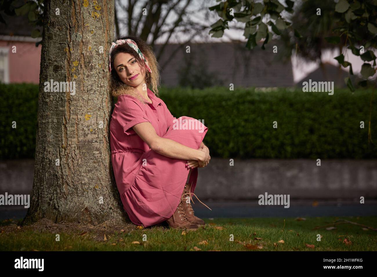 Preise blonde Frau mit lockigem Haar sitzt auf dem Stamm eines Baumes in schönen rosa Pin-up-Kleid. Stockfoto