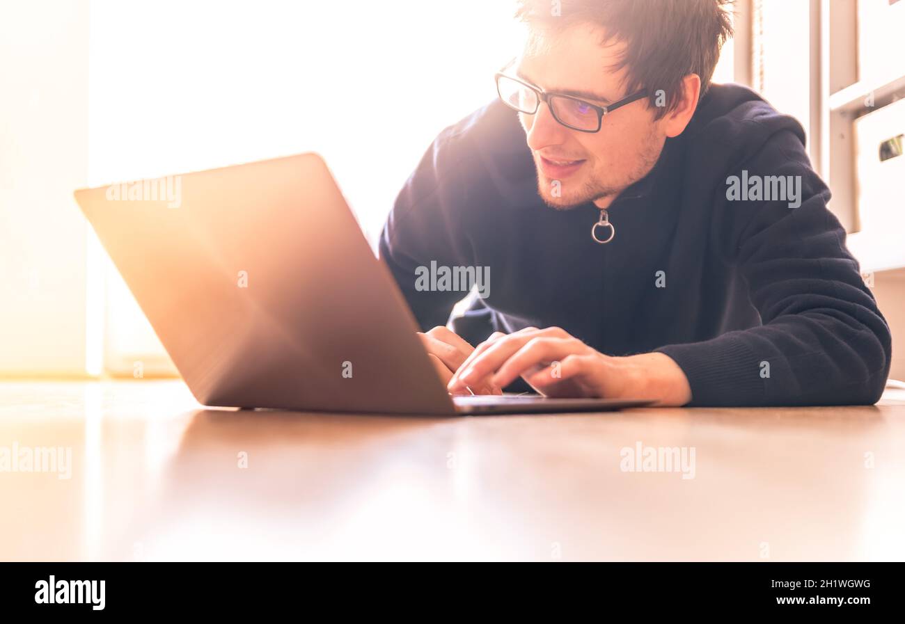 Glückliche junge Mann mit einem Laptop arbeitet auf dem Holzboden, Licht aus dem Fenster kommt Stockfoto
