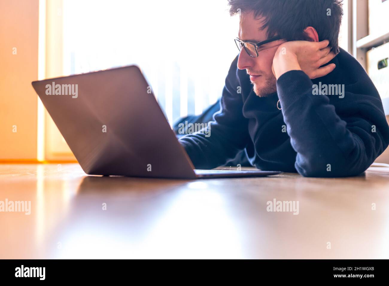 Junger Mann mit einem Laptop arbeitet auf dem Holzboden, Licht aus dem Fenster kommt Stockfoto