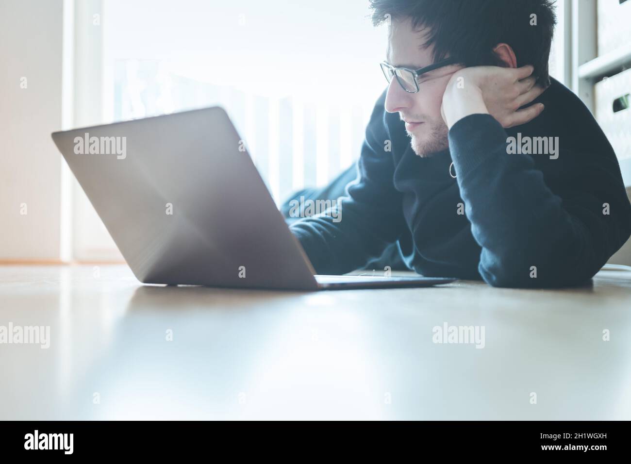 Junger Mann mit einem Laptop arbeitet auf dem Holzboden, Licht aus dem Fenster kommt Stockfoto