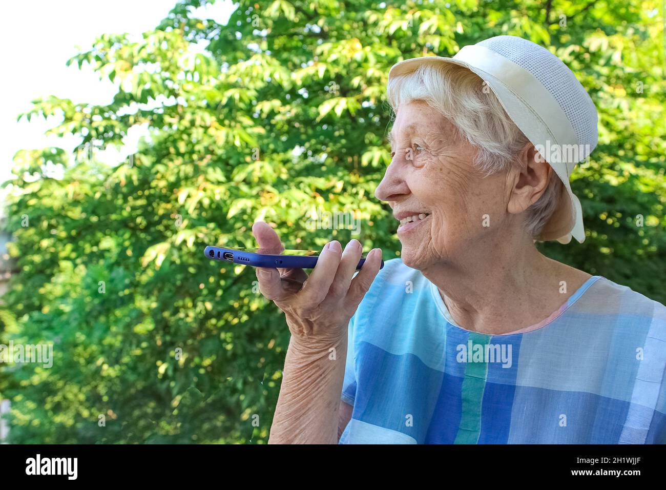 Charmante ältere Frau in rechteckiger, schwarz umrandter Brille mit Spracherkennungsfunktion auf dem Handy. Moderne ältere weibliche Holding elektronische gad Stockfoto