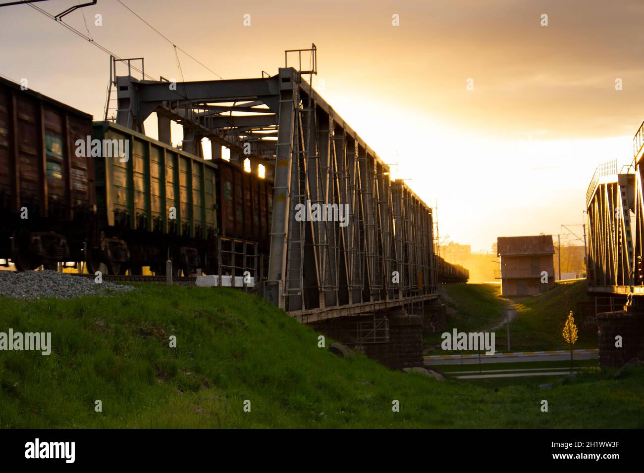 Selektiver Fokus. Güterwagen auf einer Eisenbahnbrücke, die von einem Zug gezogen wird. Abendsonne und die Reflexion des orangen Abendlichts aus der Metallstruktur Stockfoto