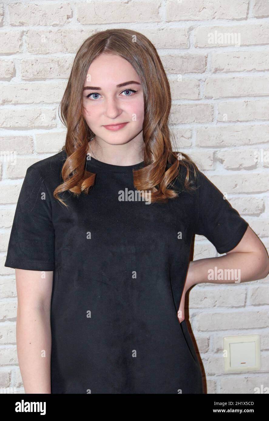 Mädchen mit üppiger Frisur posiert auf Backstein Wand Hintergrund. Porträt des Mädchens in schwarzem Kleid. Frisur. Teenager-Mädchen mit schönen Locken der Haare. Mädchen Stockfoto