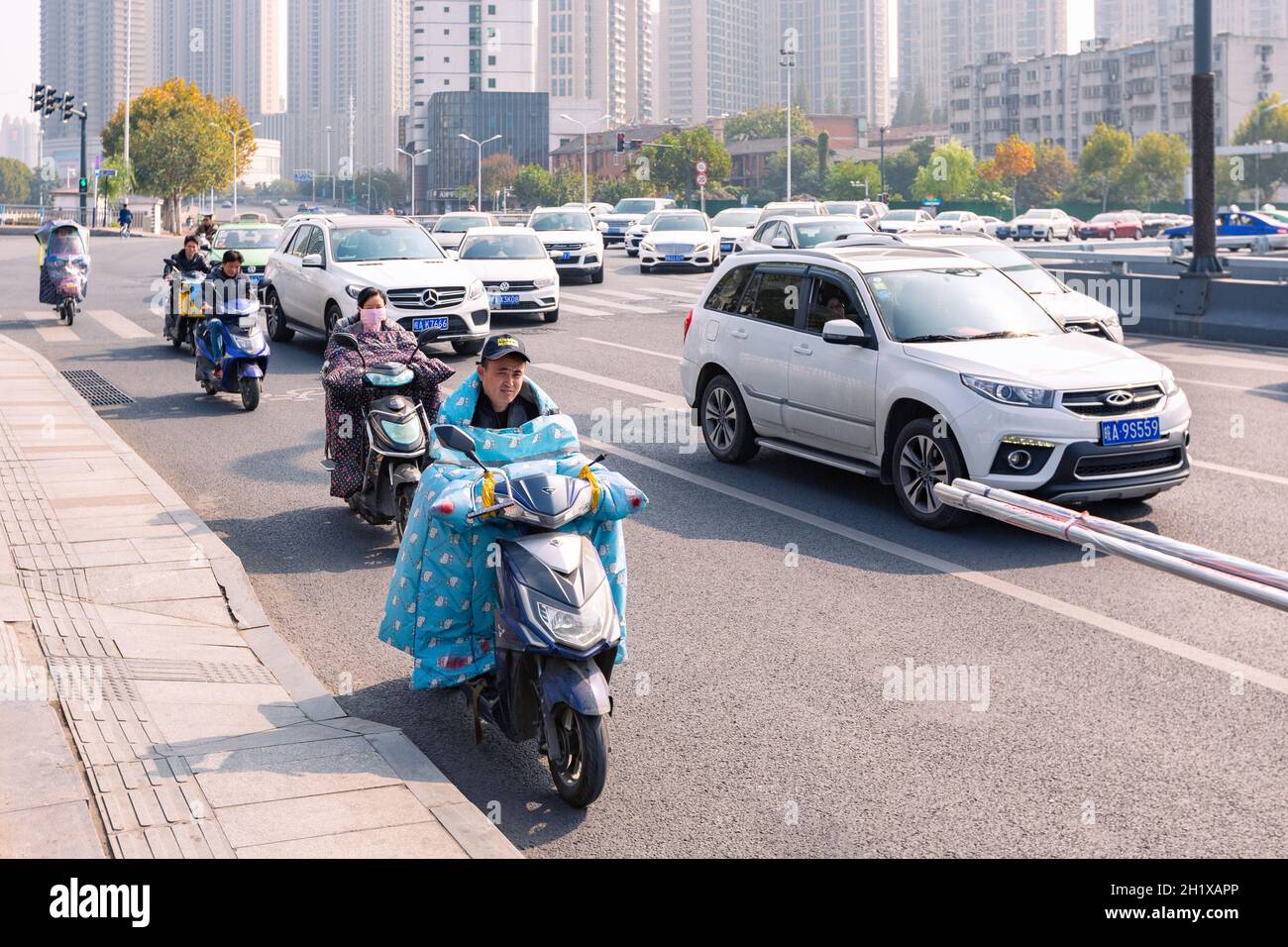 Hefei, China - 5. November 2019: Menschen mit Elektrofahrrädern auf der Kreuzung. Das Wetter wurde kalt und jedes Elektrofahrrad war mit buntem Wind ausgestattet Stockfoto