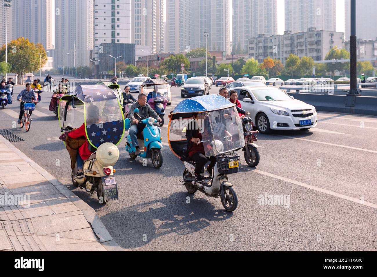 Hefei, China - 5. November 2019: Menschen mit Elektrofahrrädern auf der Kreuzung. Das Wetter wurde kalt und jedes Elektrofahrrad war mit buntem Wind ausgestattet Stockfoto