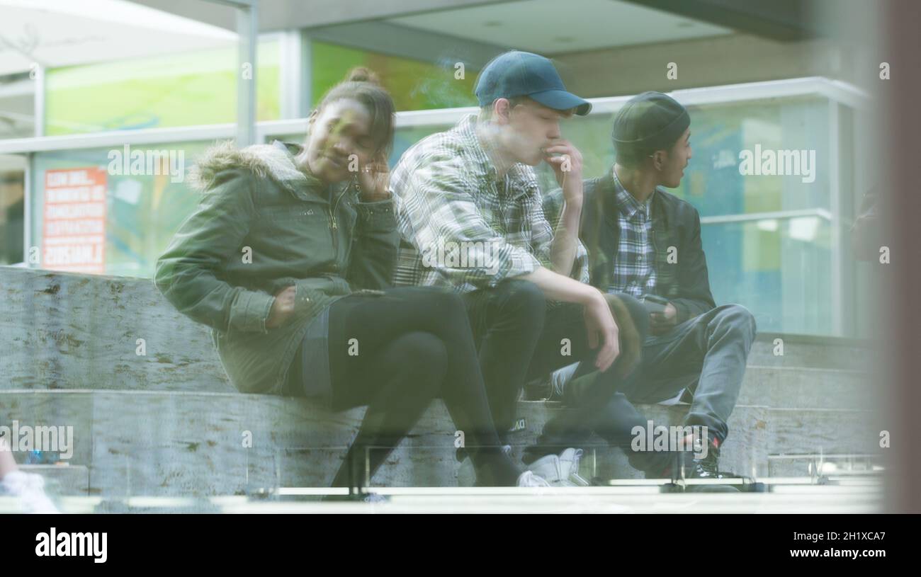 Eine Gruppe von Freunden, die auf der Treppe sitzen und draußen rauchen Stockfoto