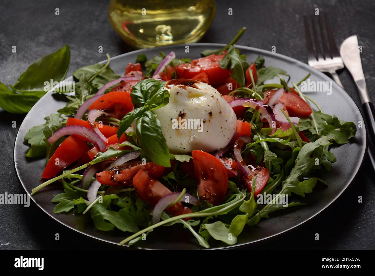 Salat mit Tomaten und Burrata-Käse mit Basilikum und Olivenöl auf dunklem Hintergrund. Traditionelles italienisches Gericht Burrata-Käse. Burrata serviert mit tomat Stockfoto