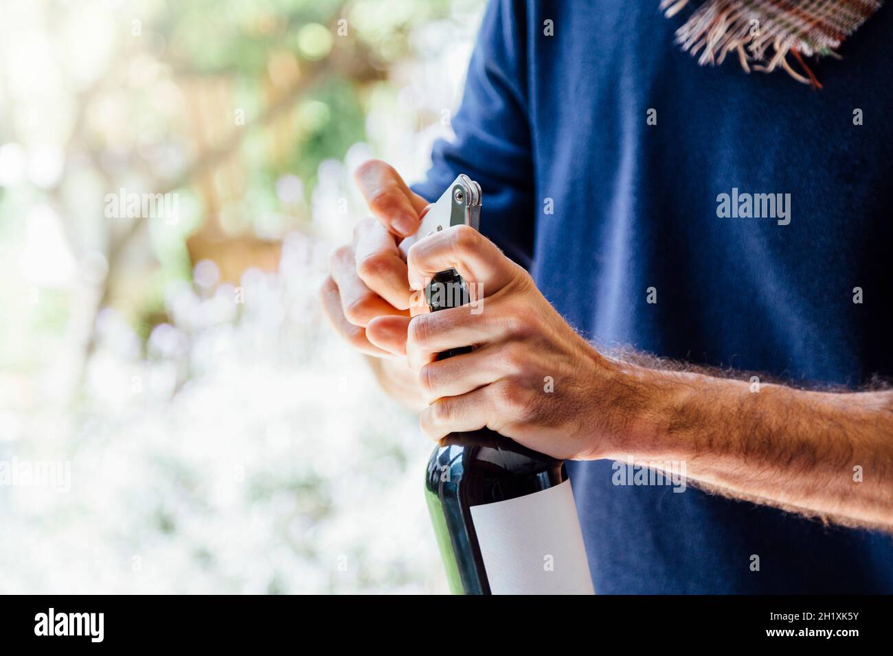 Ein junger Mann, der eine Flasche Rotwein mit einem Korkenzieher öffnet. Asado-Tag in Argentinien. Stockfoto
