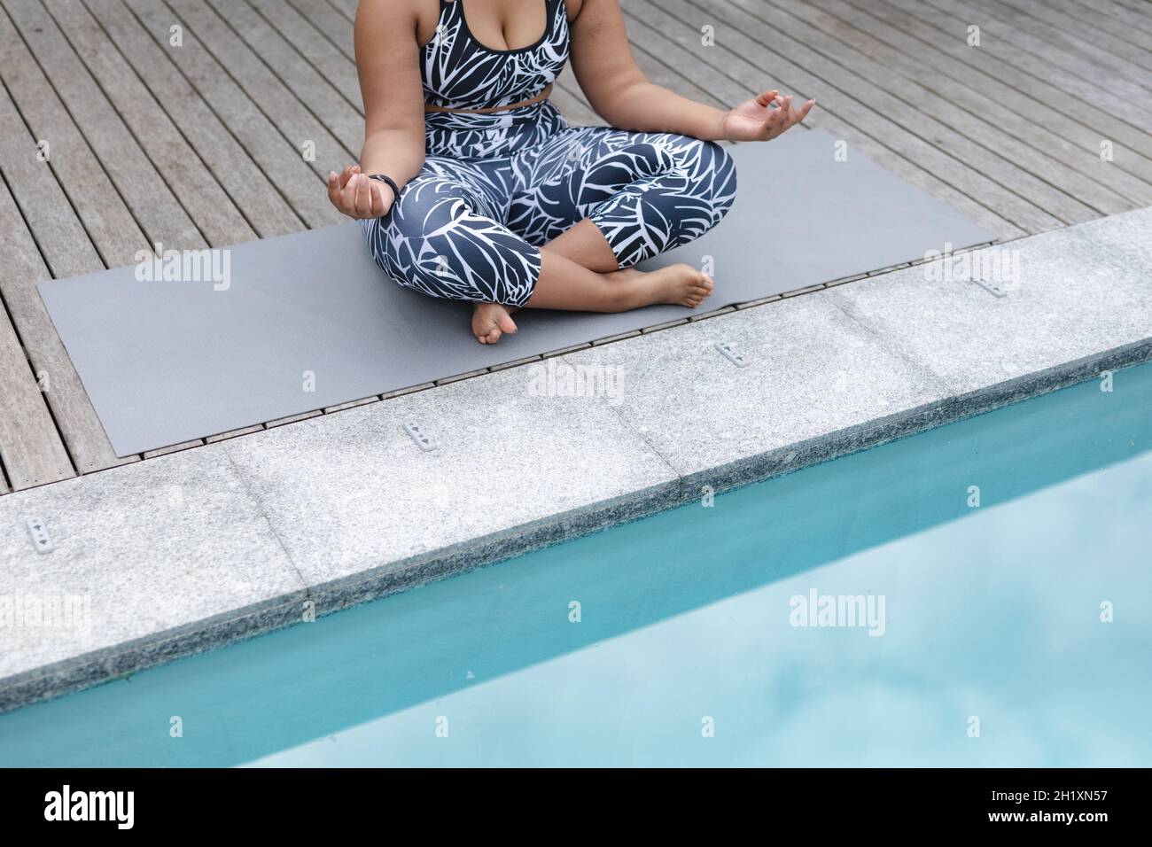 Eine afroamerikanische plus große Frau, die auf einer Matte im Garten am Pool Yoga praktiziert Stockfoto