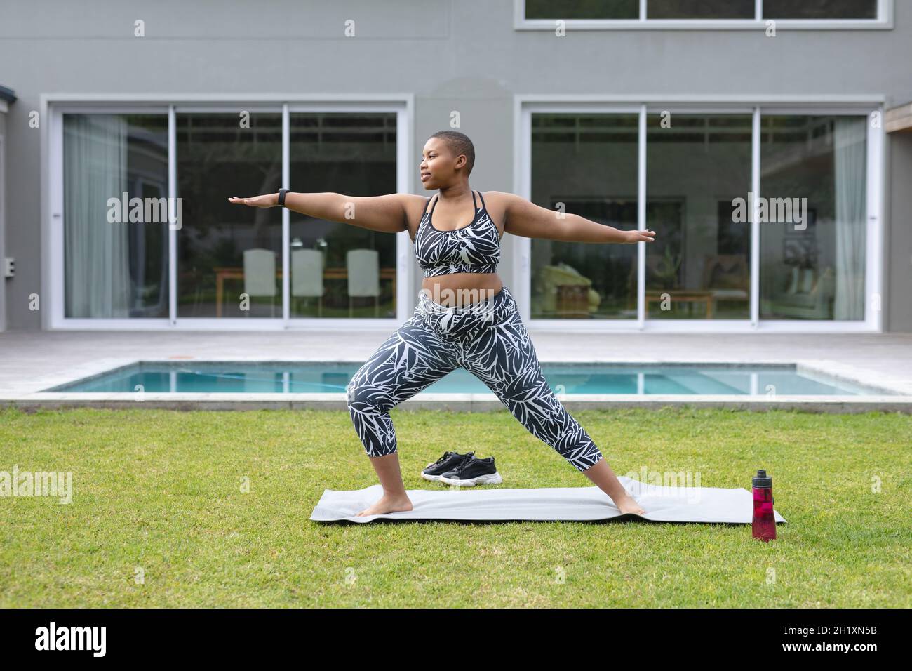 Fokussierte afroamerikanische plus size Frau, die Yoga auf einer Matte im Garten am Pool praktiziert Stockfoto