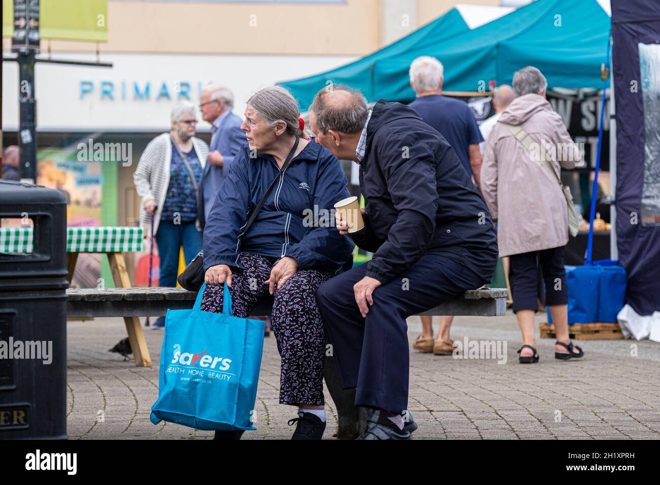 Ein reifes Paar, das auf einer Bank auf einem Straßenmarkt in Lemon Quay in Truro in Cornwall sitzt. Stockfoto