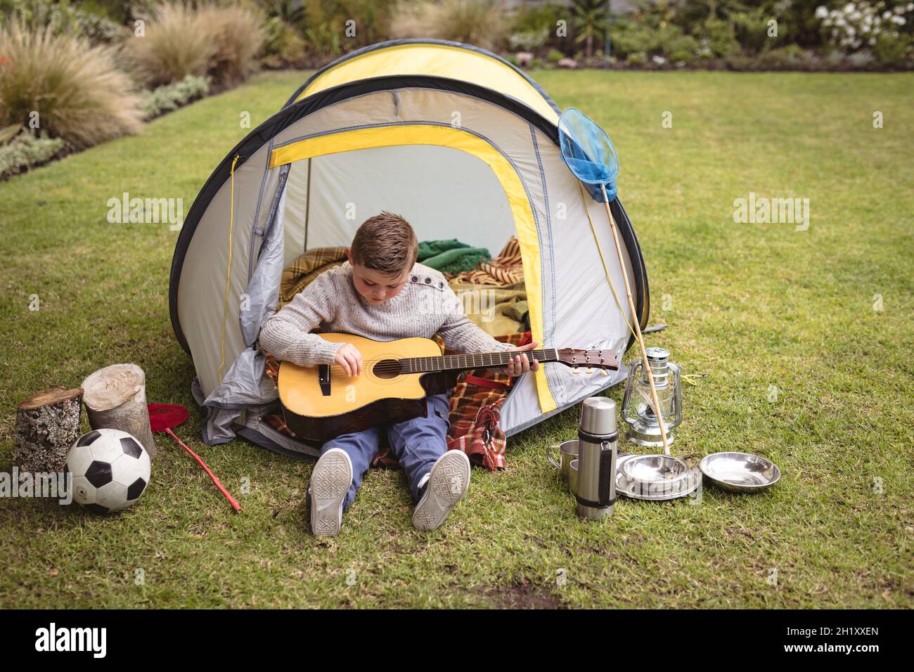 Kaukasischer Junge spielt Gitarre, während er in einem Zelt im Garten sitzt Stockfoto