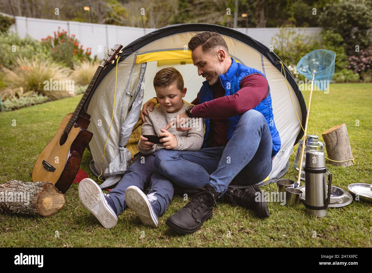 Kaukasischer Vater und Sohn mit Smartphone, während sie in einem Zelt im Garten sitzen Stockfoto