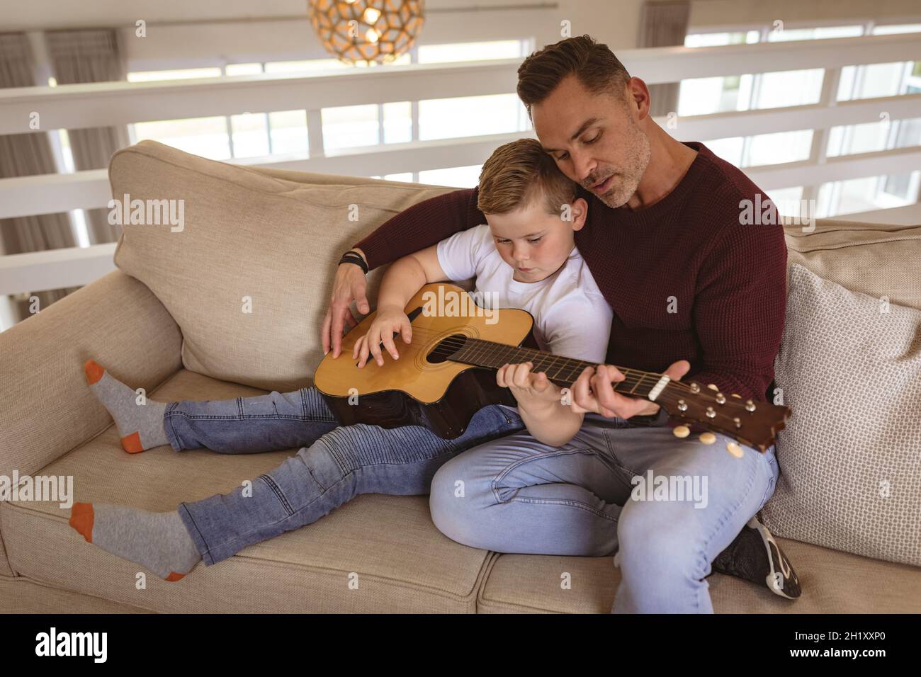 Der kaukasische Vater lehrt seinen Sohn, Gitarre zu spielen und sitzt zu Hause auf der Couch Stockfoto