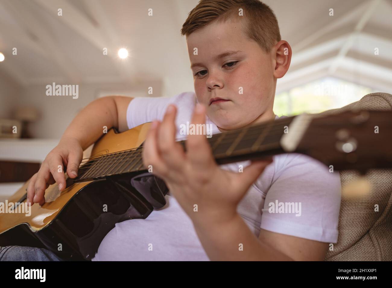 Nahaufnahme des kaukasischen Jungen, der Gitarre spielt und zu Hause auf der Couch sitzt Stockfoto