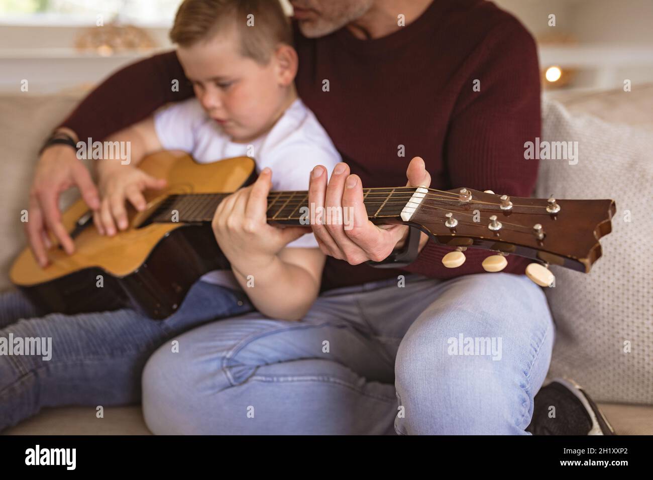 Mittlerer Abschnitt des kaukasischen Vaters, der seinem Sohn beibrachte, Gitarre zu spielen, sitzend auf der Couch zu Hause Stockfoto