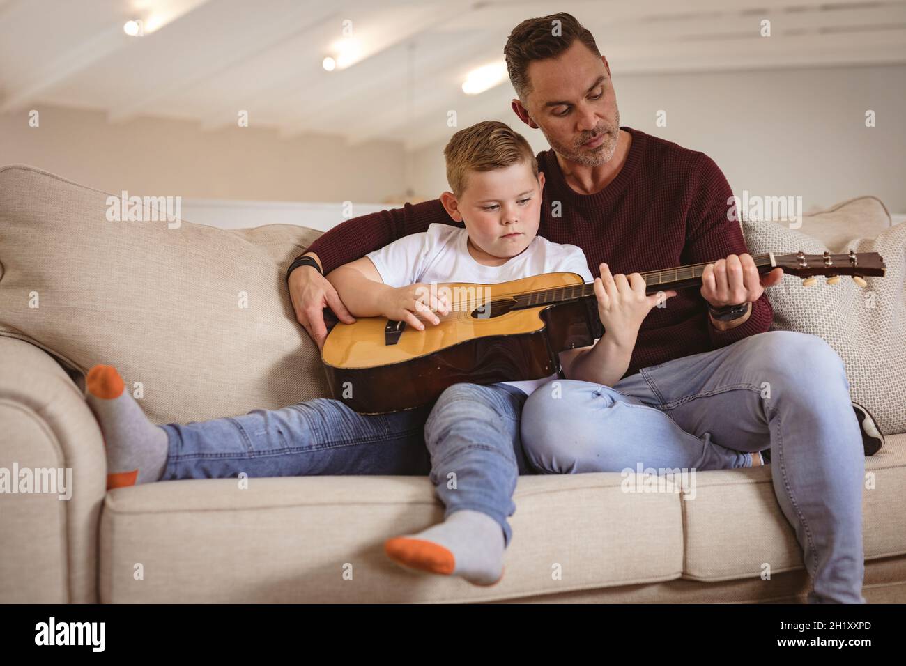 Der kaukasische Vater lehrt seinen Sohn, Gitarre zu spielen und sitzt zu Hause auf der Couch Stockfoto