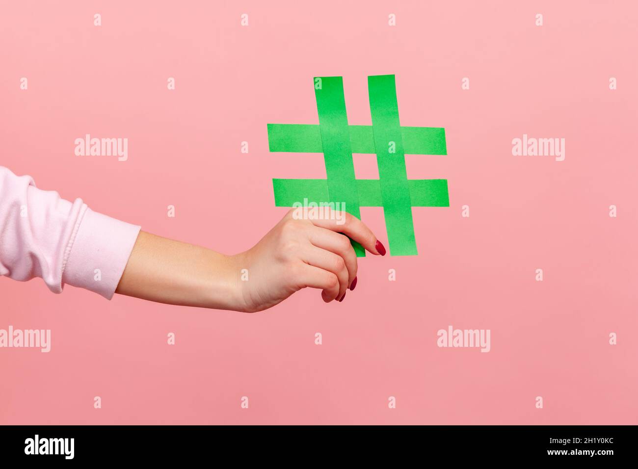 Nahaufnahme von gelbem Hash-Zeichen, weiblicher Hand mit Papier-Hashtag, Symbol für Trends in sozialen Netzwerken und beliebte Kommentare, berühmter Blog-Inhalt, Promotion. Innenaufnahme des Studios isoliert auf rosa Hintergrund Stockfoto
