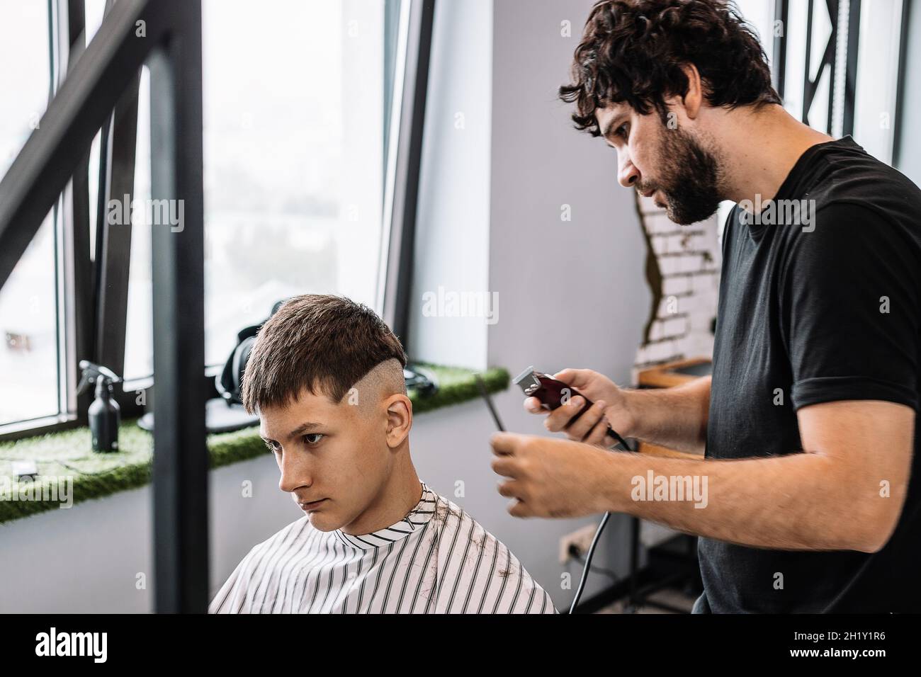 Stylish Barber macht einen modischen Haarschnitt für einen jungen Kerl. Professionelle Männerrasur und Haarschnitt in einem Friseursalon oder Friseursalon. Haarpflege Stockfoto
