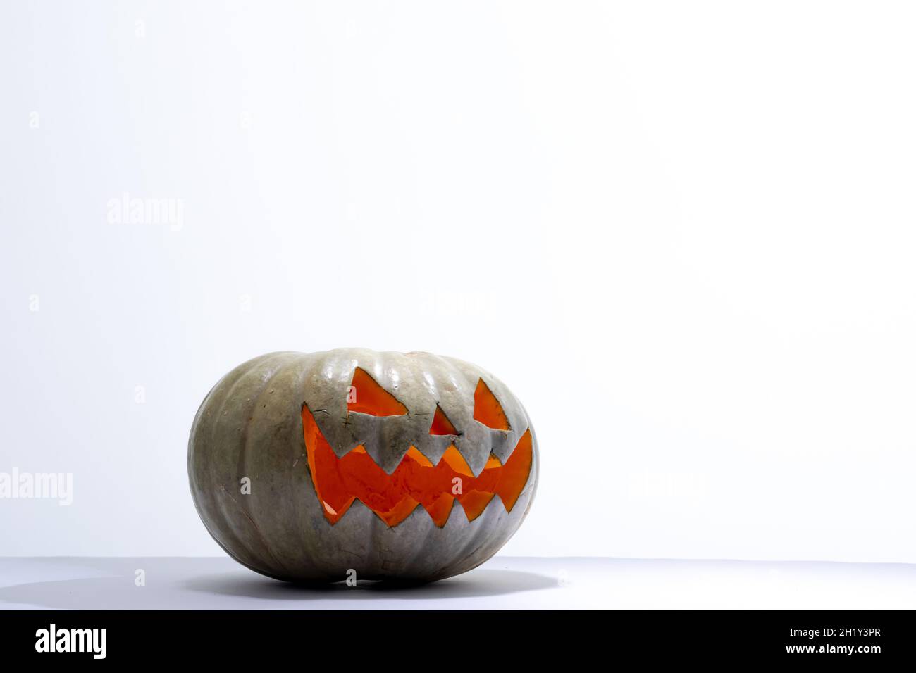 Komposition von beleuchteten gruseligen halloween geschnitzten grünen Kürbis auf weißem Hintergrund Stockfoto