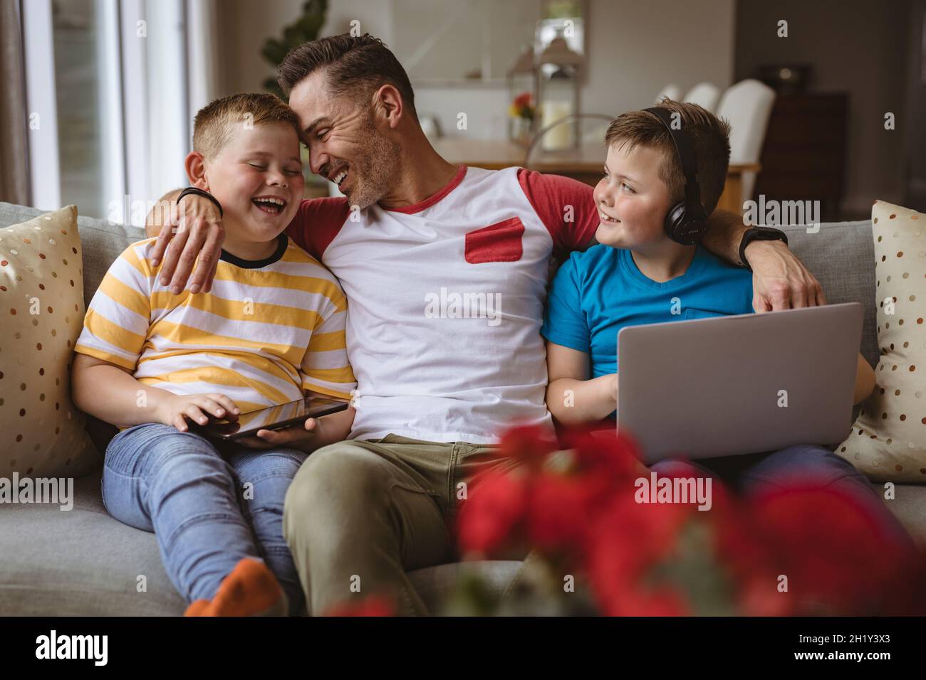 Porträt eines kaukasischen Vaters und zweier Söhne mit Laptop und digitalem Tablet, die zu Hause lächeln Stockfoto