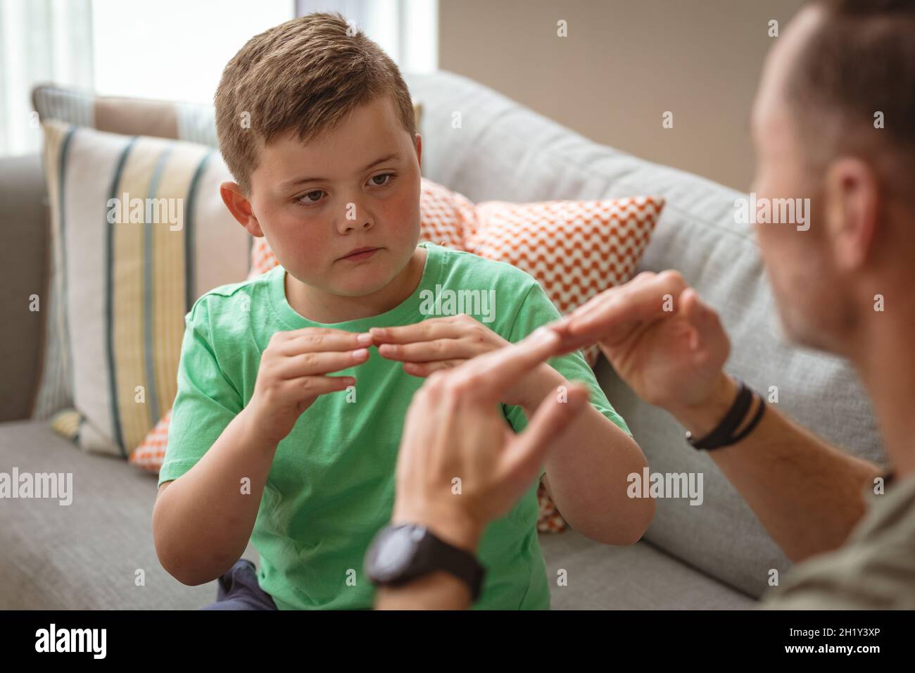 Kaukasischer Vater und Sohn kommunizieren mit Gebärdensprache, während sie zu Hause auf der Couch sitzen Stockfoto