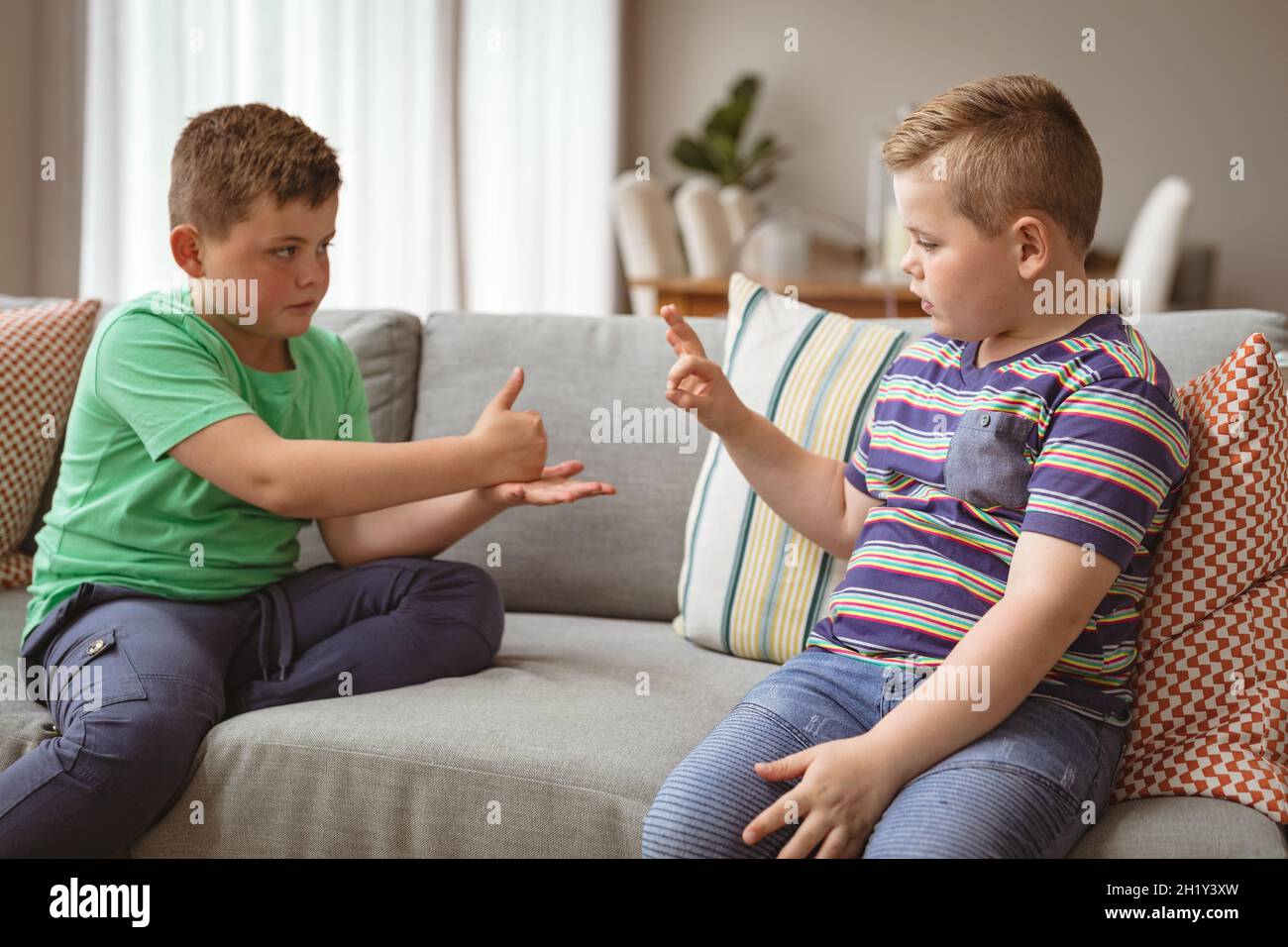 Zwei kaukasische Jungen, die sich mit Gebärdensprache verständigen, während sie zu Hause auf der Couch sitzen Stockfoto