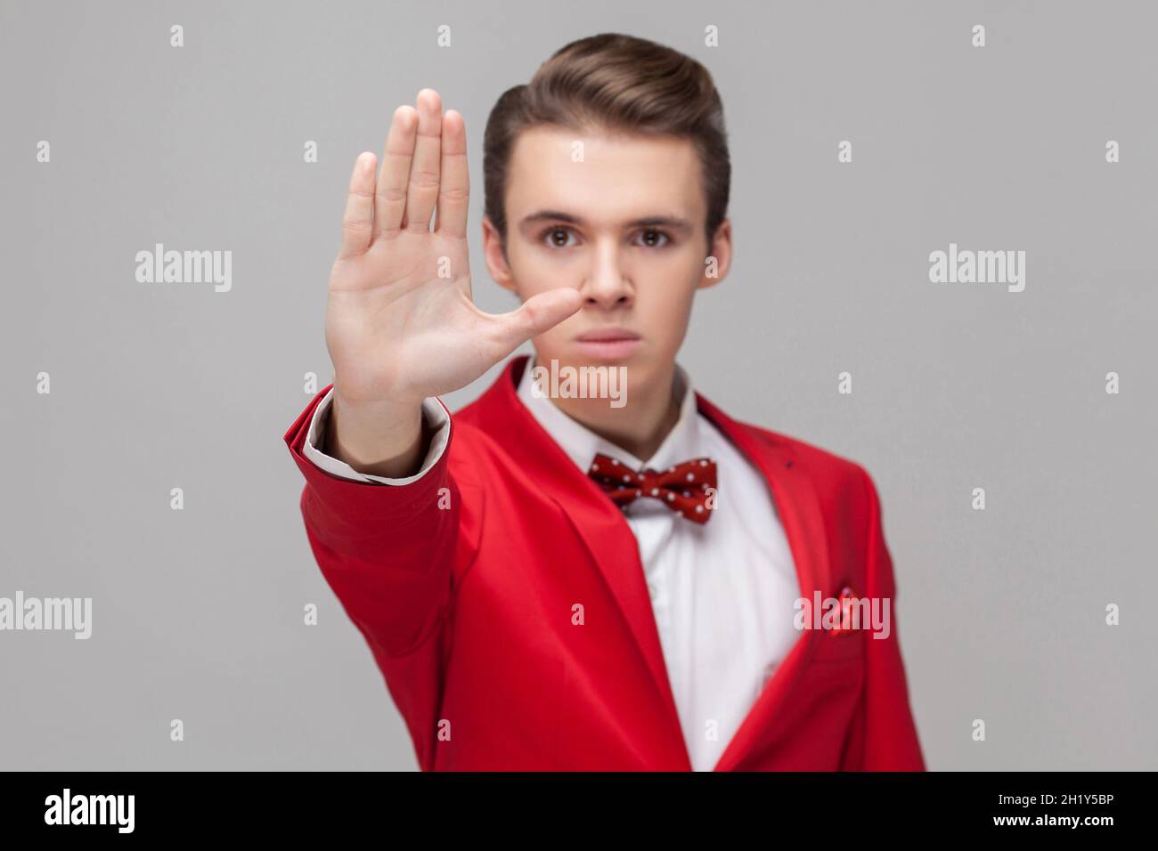 Stopp. Porträt eines selbstbewussten Gentleman mit stilvoller Frisur in rotem Smoking und Fliege mit Verbotshandgesten, Nein sagen, verboten, Konzept leugnen. Innenaufnahme Studio isoliert, grauer Hintergrund Stockfoto