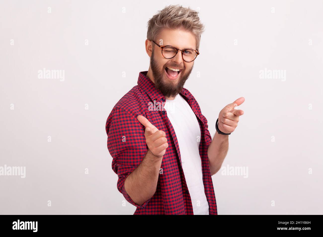 Porträt von zufrieden bärtigen Männchen in Brillen lächelnd und zwinkert vor der Kamera, gestikulierend hey Sie unterschreiben. Innenaufnahme des Studios isoliert auf grauem Hintergrund Stockfoto