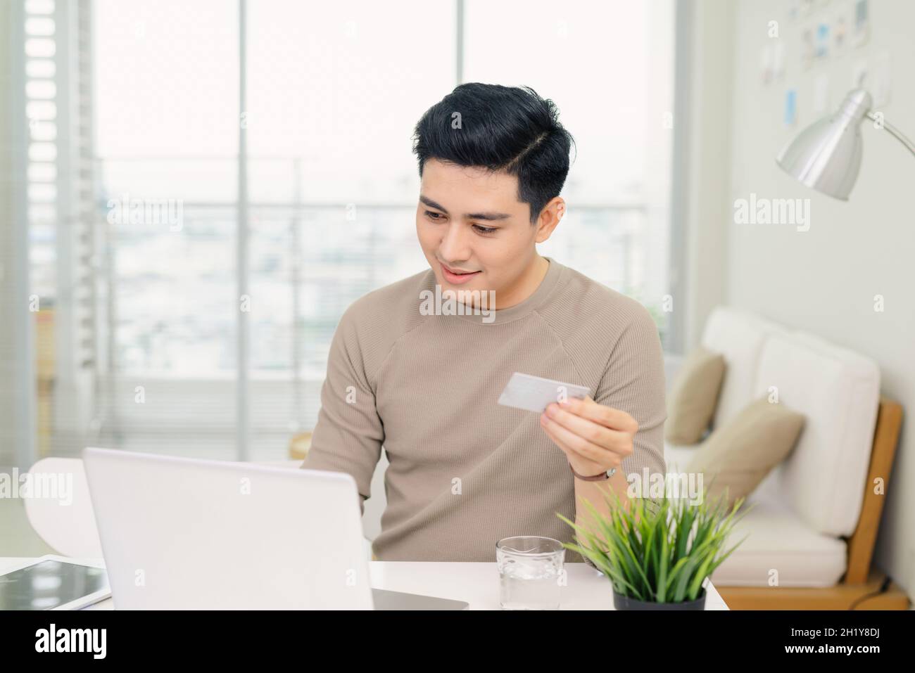 Hübscher junger Geschäftsmann, der einen Computer benutzt, während er eine Kreditkarte in einem Heimbüro hält Stockfoto