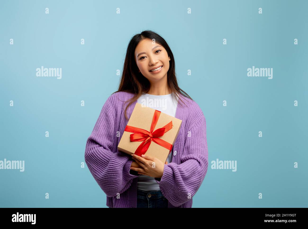 Junge asiatische Dame mit Geschenkbox und lächelnd vor der Kamera über blauem Studiohintergrund, freiem Platz Stockfoto