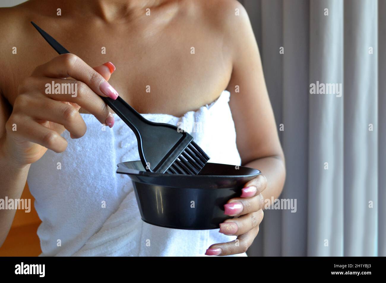 Eine Dame mischt Haarfarbeninhalte mit einer Schüssel und einem Pinsel, um ihr Haar zu Hause zu malen Stockfoto