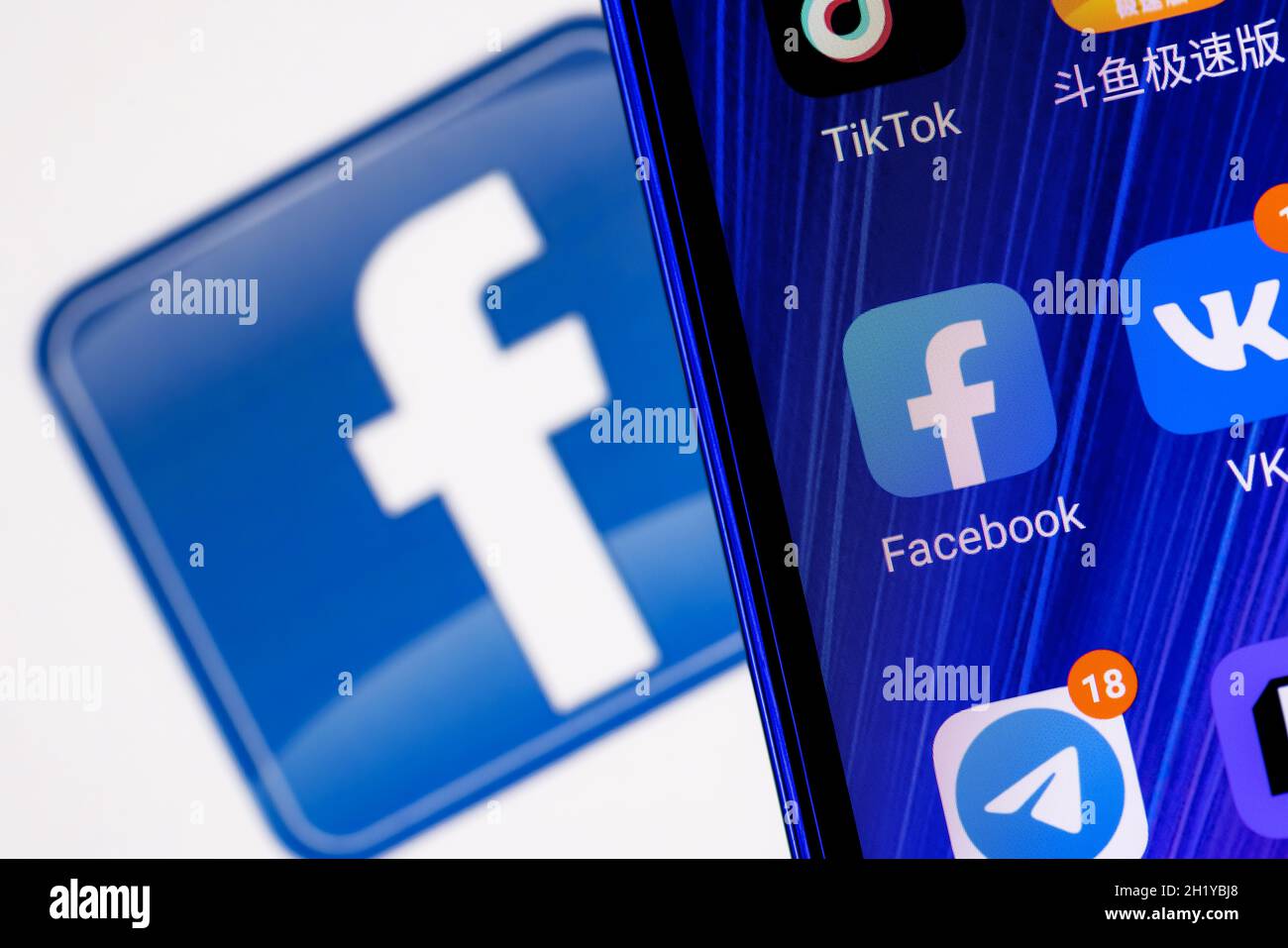 Das Symbol der Facebook-Anwendung für soziale Netzwerke unter anderem auf dem Smartphone-Bildschirm. Auf dem Hintergrund ist das Facebook-Logo zu sehen. Stockfoto