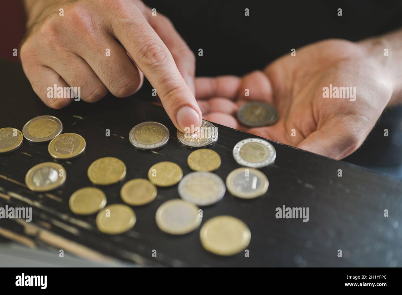 Geschäftsmann zählt Geld. Reiche männliche Hände halten und zählen Münzen verschiedener Euros auf dem Tisch vor einem Laptop Stockfoto