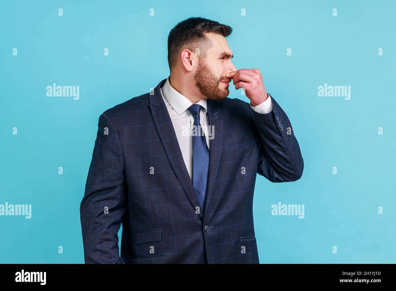 Schlechter Geruch. Porträt eines bärtigen Mannes im Anzug, der den Atem anhält und vor Abscheu grimazing, Abstoßung zum Gestank, fart Gase, unerträglichen Geruch ausdrückt. Innenaufnahme des Studios isoliert auf blauem Hintergrund. Stockfoto