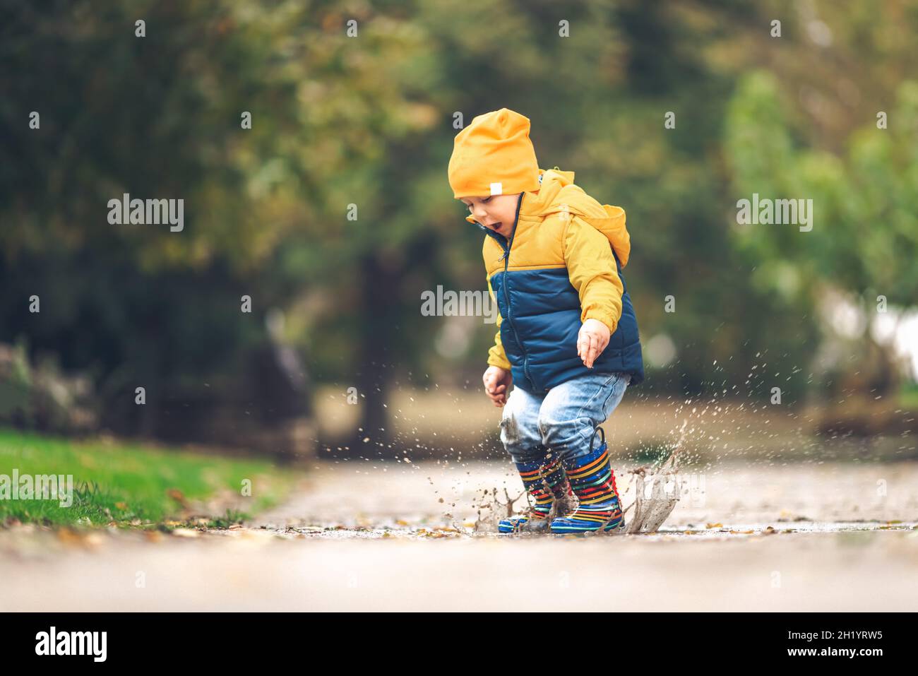 Glücklicher kleiner Junge, der im Herbst auf einer verregneten Pfütze auf die Natur springt Stockfoto