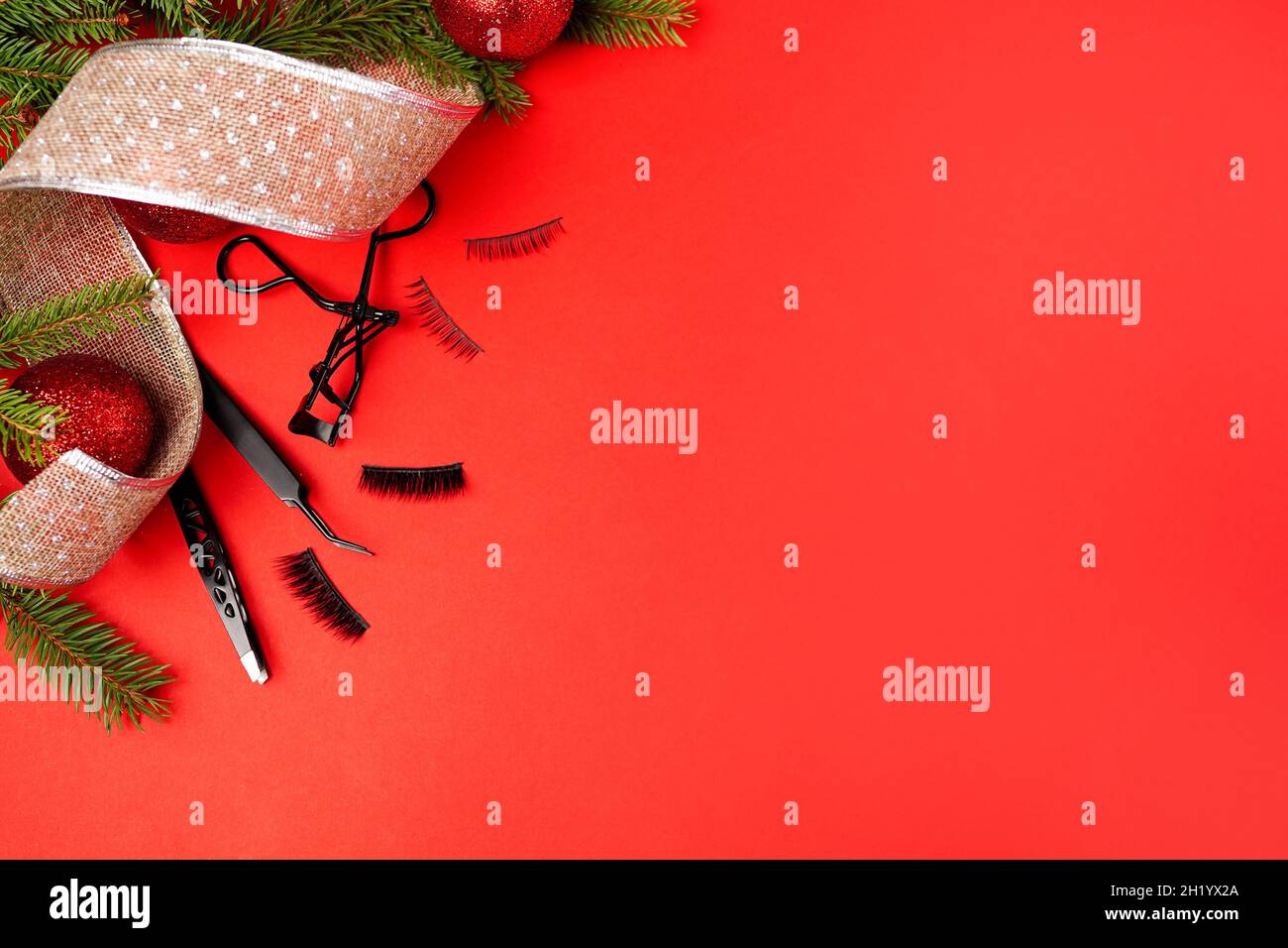 Falsche Wimpern mit weihnachtsschmuck auf rotem Hintergrund. Make-Up-Konzept Stockfoto