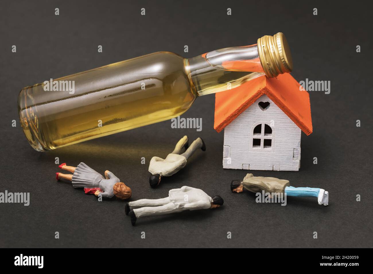 Spielzeugmänner aus Kunststoff, ein kleines Haus und eine Flasche Whiskey auf dunklem Hintergrund, ein Konzept zum Thema Alkoholmissbrauch Stockfoto