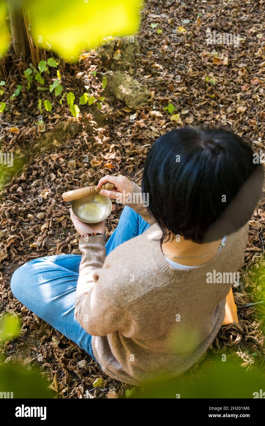 Obere vertikale Ansicht der Frau, die auf einer tibetischen Klangschale zur Klangtherapie in der Natur spielt. Stockfoto