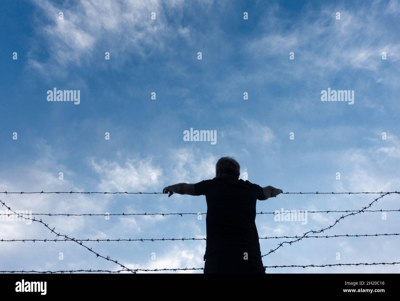 Rückansicht eines Mannes mit Händen auf Stacheldraht, Stacheldrahtzaun. Stockfoto