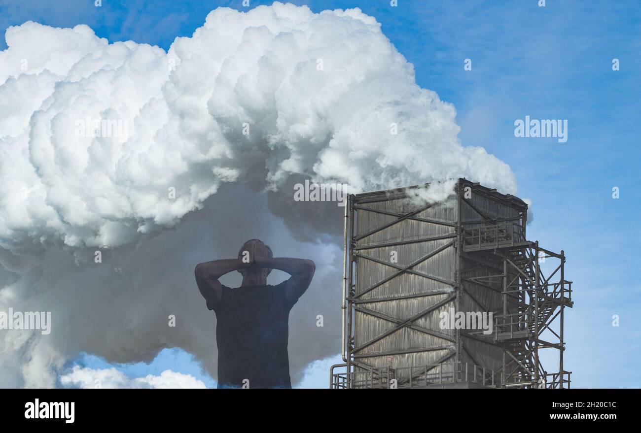 Globale Erwärmung, Konzept des Klimawandels. Mann mit den Händen über dem Gesicht mit dem Fabrikschornstein, der Rauch aufsticht. Stockfoto