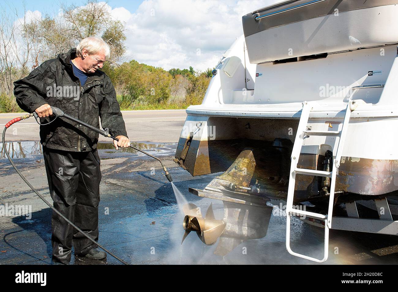 Kaukasischer Mann, der den Propeller eines Motorbootes mit einem Hochdruckreiniger wäscht Stockfoto
