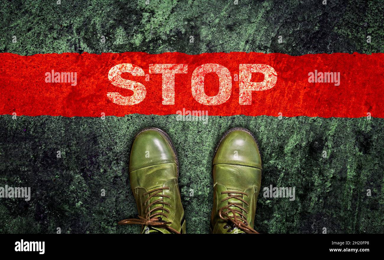 Das Wort "Stop" auf dem Asphalt vor deinen Füßen in grünen Stiefeln. Blick von oben. Stopplinie. Stockfoto