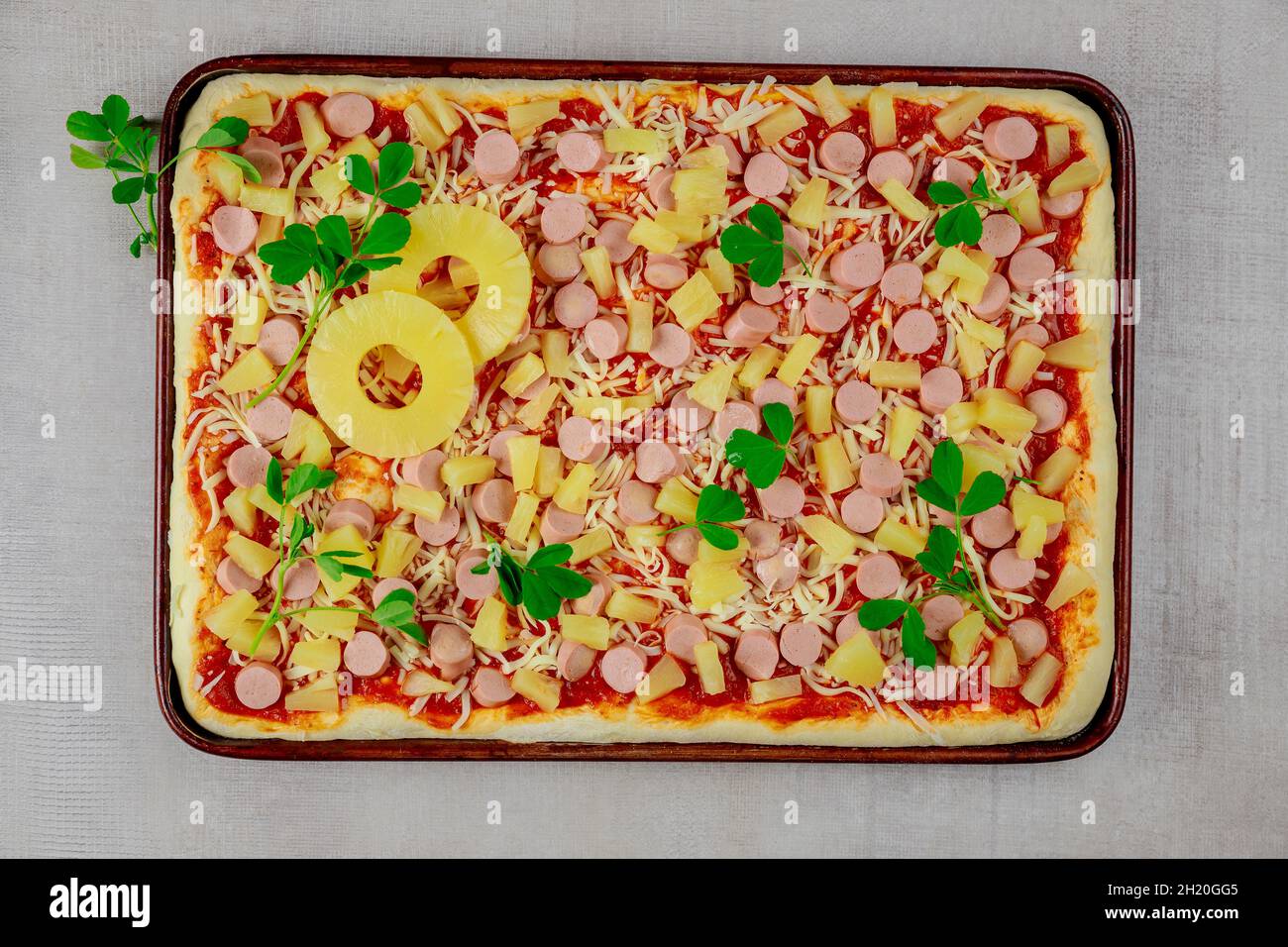 Hawaiianische Pizza mit Wurst und Ananasscheiben auf der Pfanne. Stockfoto