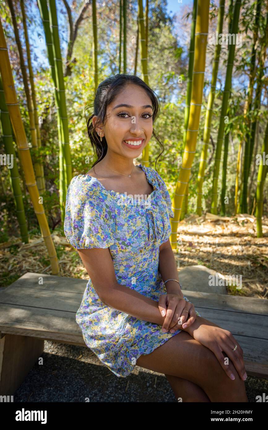 Junge, multirassische College-Studentin, die auf einer Holzbank in der Nähe eines Bambuswaldes sitzt Stockfoto