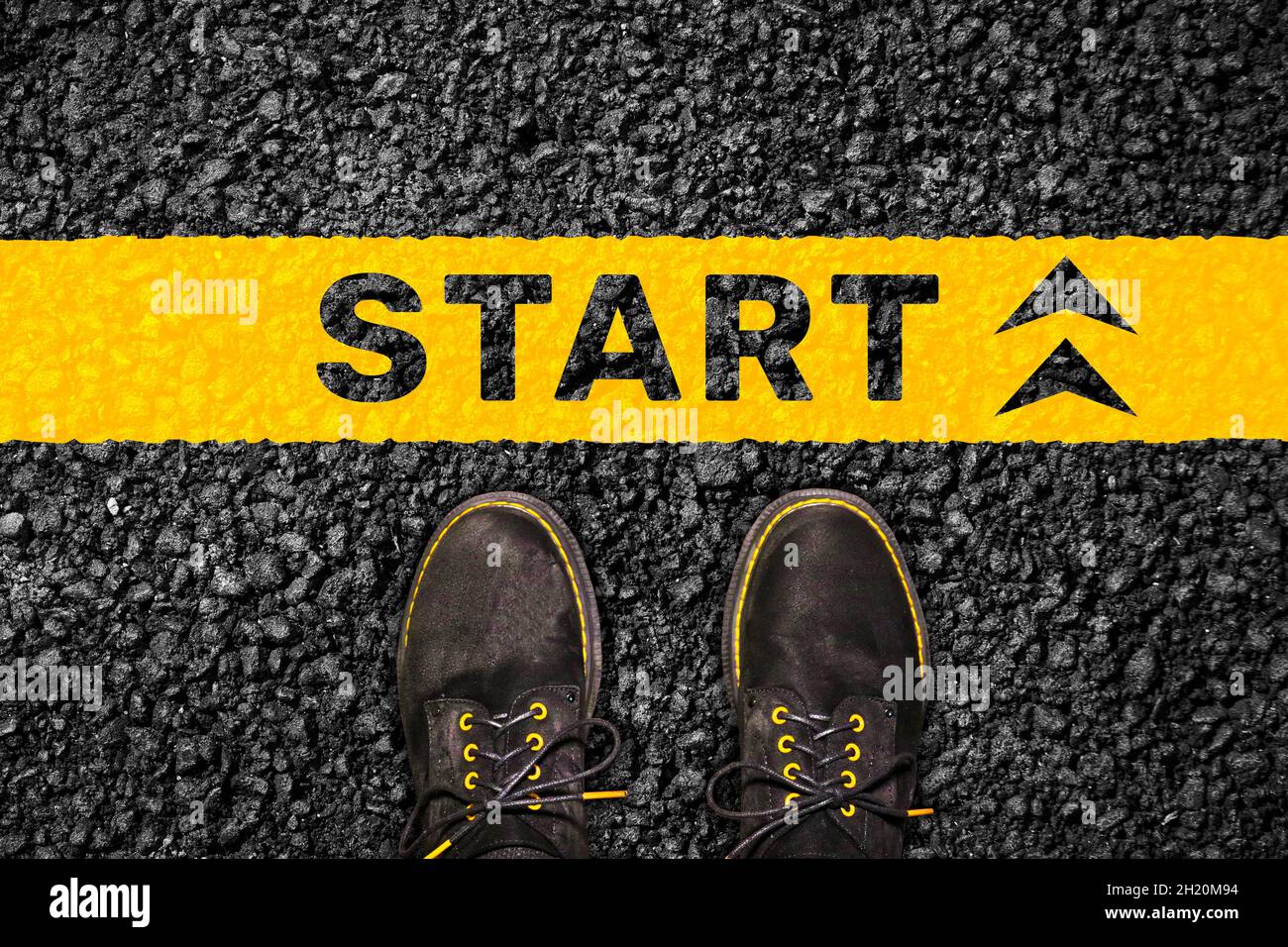 Das Konzept von Motivation und Erfolg - das Wort 'Start' auf dem Asphalt vor den Füßen in schwarzen Stiefeln. Blick von oben. Startlinie. Stockfoto