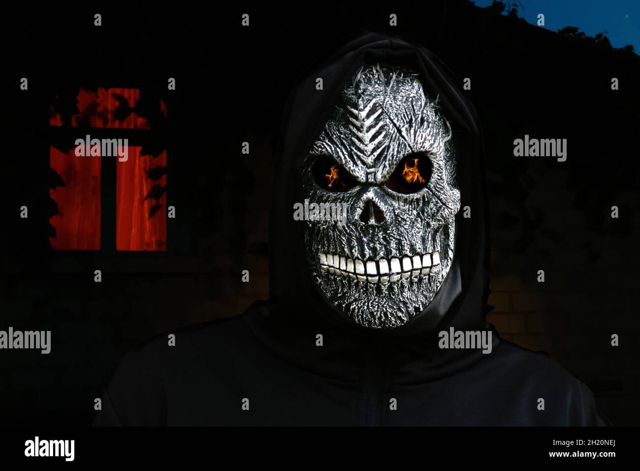 Nahaufnahme des grimmigen Reaper. Mann in Totenmaske mit Feuerflamme in den Augen auf dunklem nächtlichen Hintergrund. Faschingskostüm, gruselige Zähne. Halloween-Holida Stockfoto