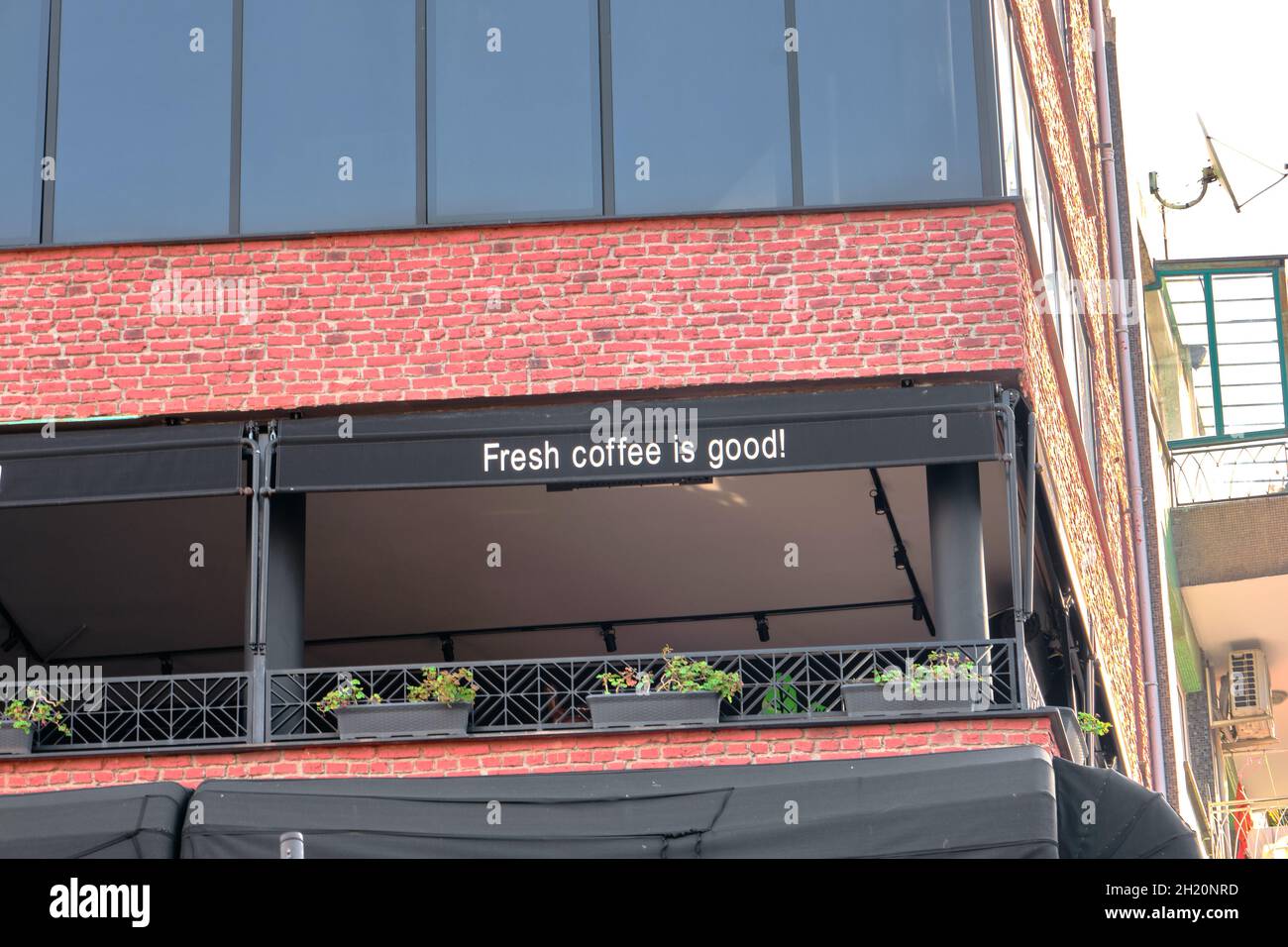 Ein wundervoller Balkon und eine Terrasse eines Cafe-Shops und es wurde geschrieben, dass „frischer Kaffee gut ist!“ Und Balkon aus roten Ziegeln und Blumen darauf. Stockfoto